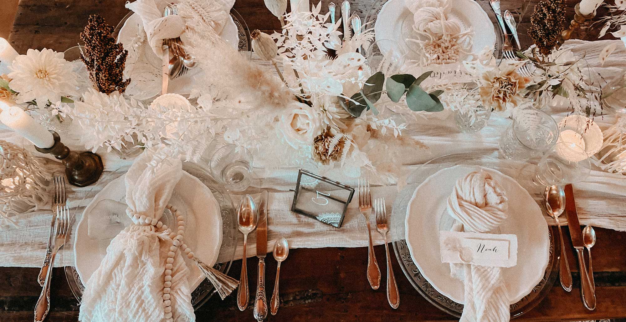 Eine Hochzeitstafel im Bohostyle, gedeckt mit Tellern, Servietten und verschiedenen Dekoelementen